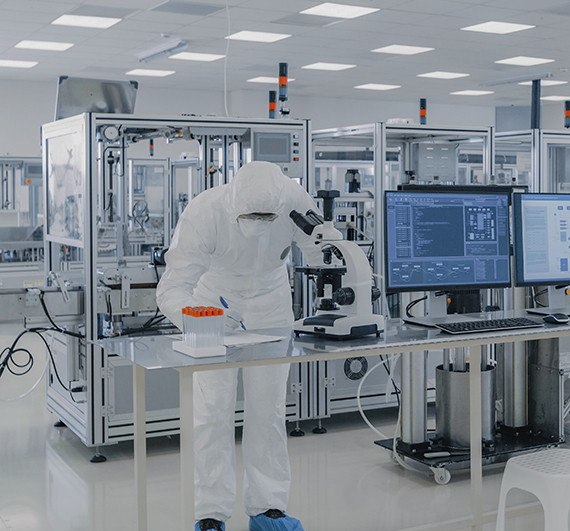 Shot of Sterile High Precision Manufacturing Laboratory where Scientists in Protective Coverall's Use Computers and Microscopes, doing Pharmaceutics, Biotechnology and Semiconductor Research.